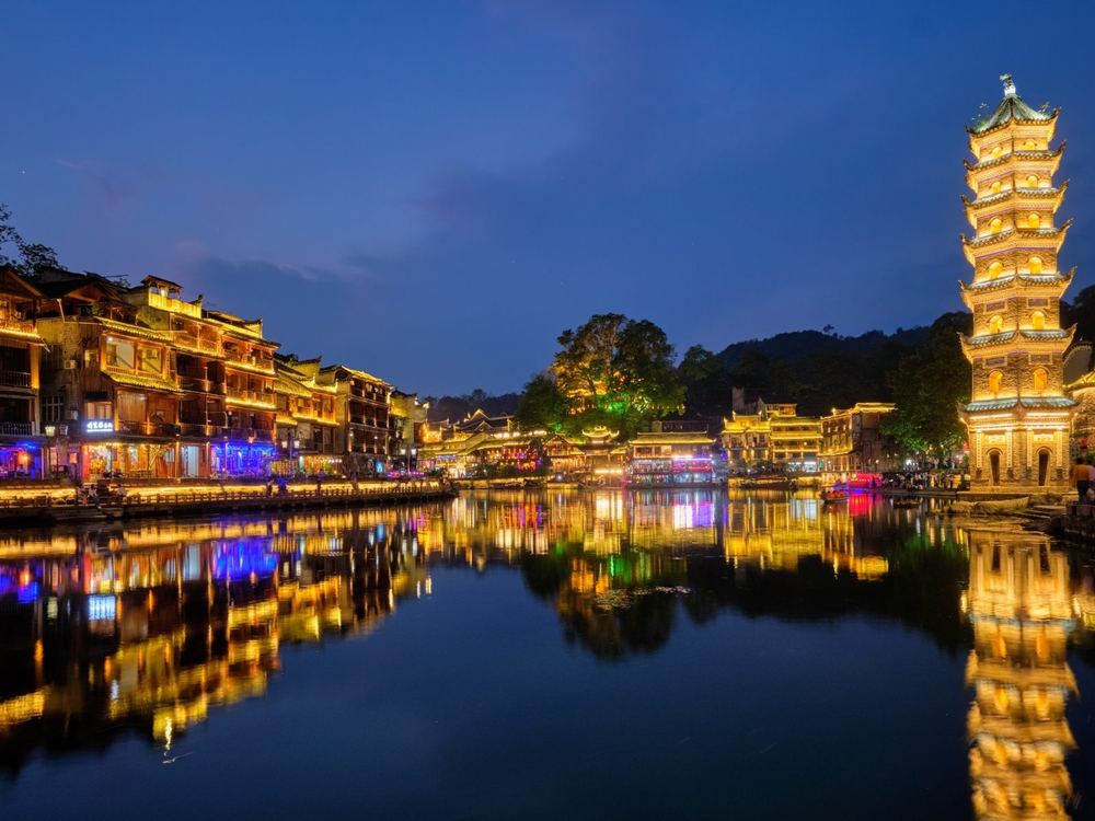 Casas sobre pilotes y pagoda iluminadas junto al río en Fenghuang